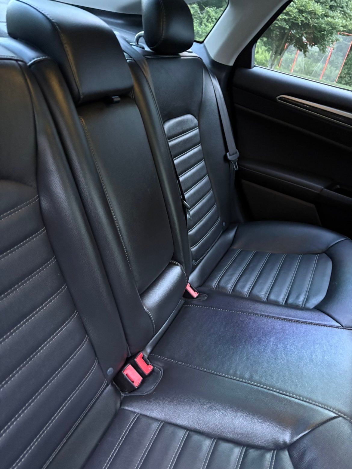 Interior of car with black leather back seats featuring horizontal stitching and red seat belt buckles